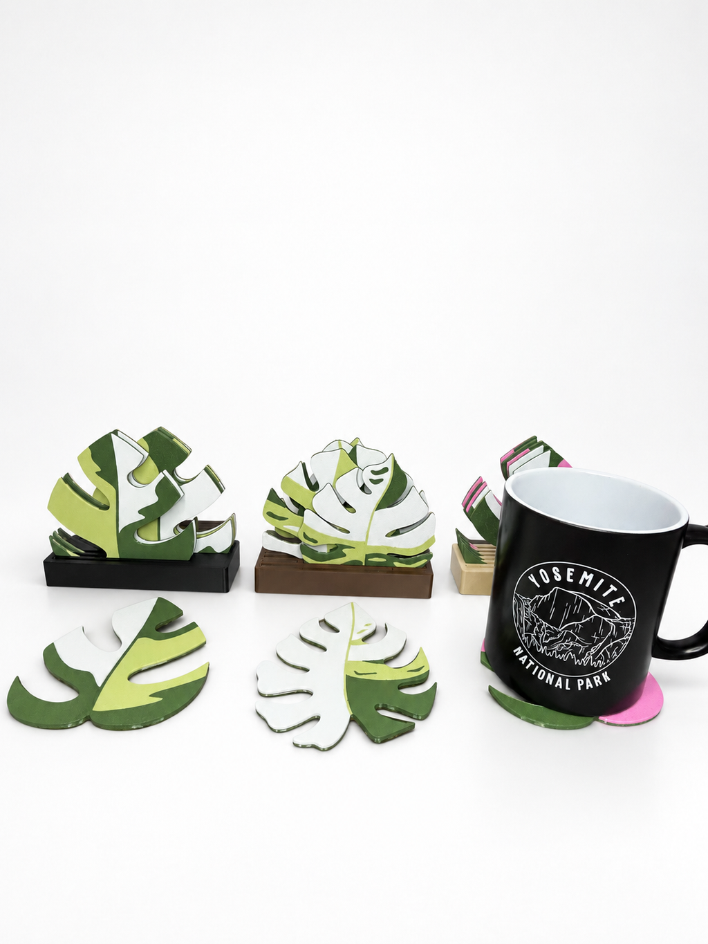 A black mug on a pink Mini Monstera coaster beside light green coaster sets on a white background. Mug not included.