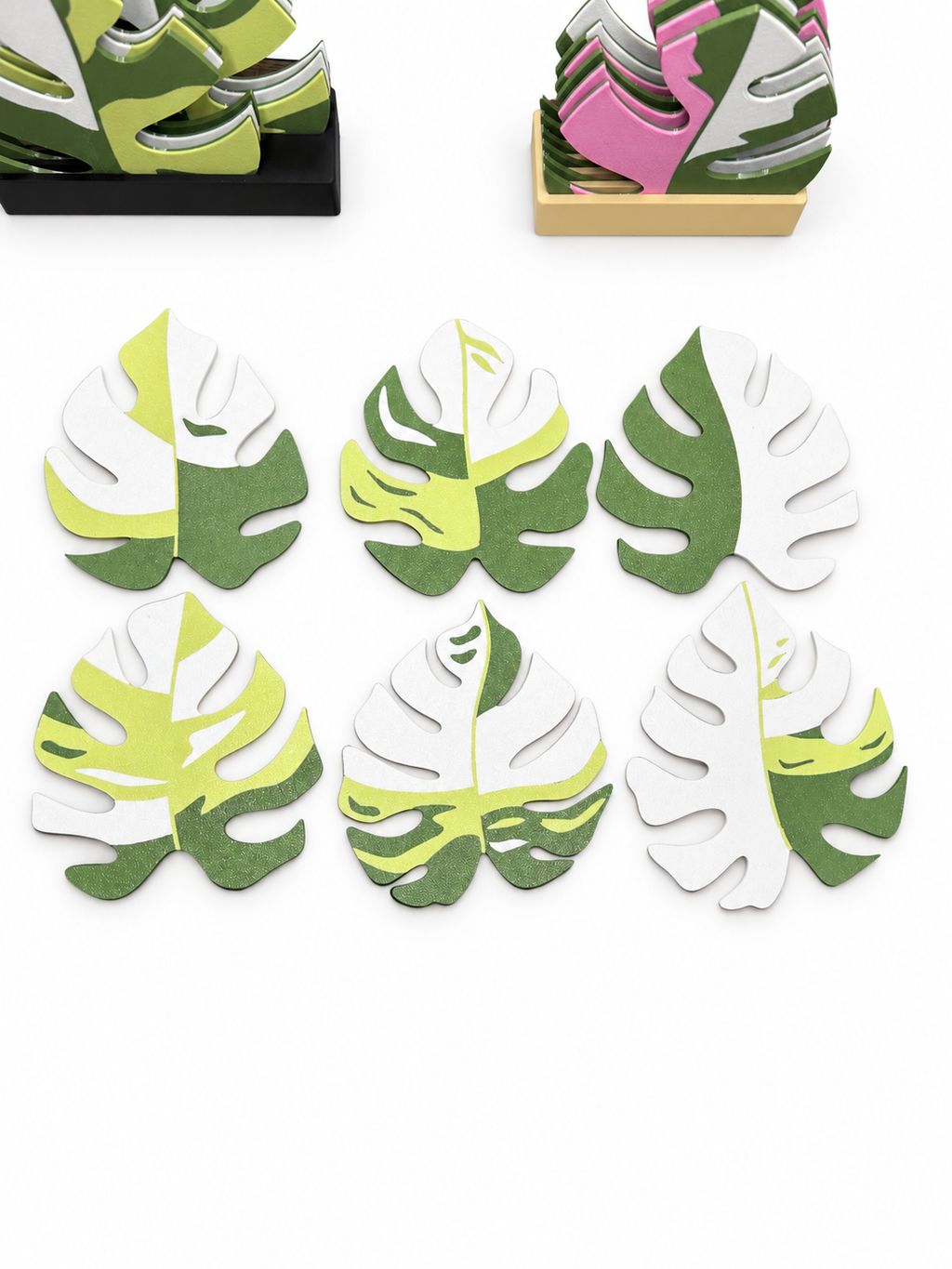Six Monstera deliciosa coasters laid flat to show their light green, forest green and white patterns, with holders in the background.
